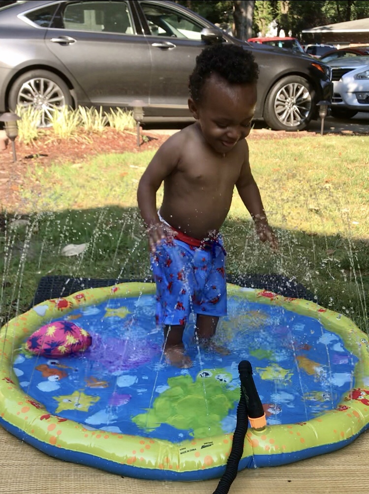 Toddler playing in splash pad with water sprinkler, toddler summer essentials